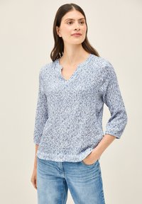 Haut en tricot texturé bleu doux avec un décolleté en V et des manches trois-quarts, présentant un motif subtil. Associé à un jean en denim bleu clair.