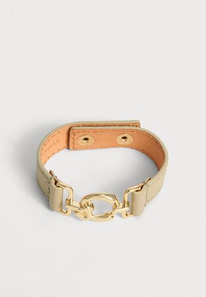 Pulsera de cuero beige con detalle de eslabones de cadena metálica dorada y cierre de botón a presión, mostrada sobre un fondo liso y claro.