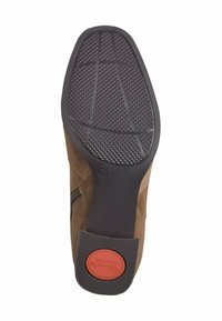 Semelle de botte de cheville en daim marron avec une adhérence en caoutchouc noir texturé et un logo de confort en caoutchouc rouge. Présente un bout arrondi et une fermeture éclair sur le côté.