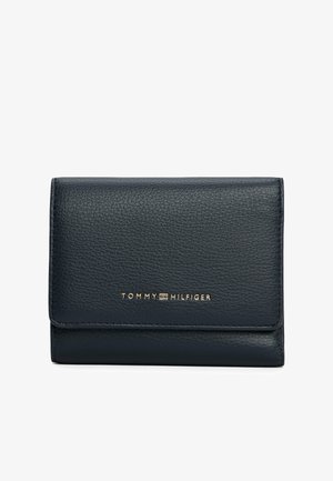 Portafoglio in pelle nera textured con logo dorato Tommy Hilfiger centrato sul risvolto anteriore, su uno sfondo bianco uniforme.
