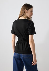 Black short-sleeve t-shirt with a gathered elastic waist, worn with blue jeans. Smooth texture, minimalistic design, and crew neckline.