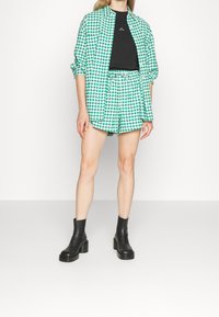 Green and white checkered shirt paired with matching shorts, black T-shirt underneath, and black ankle boots with chunky heels.