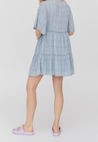 Světle modré šaty po kolena vyrobené z jemné tkaniny s krátkými rukávy, s vrstveným designem a krajkovými detaily. Nosené s levandulovými nazouvacími sandály.