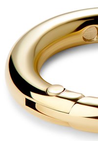 Gylden metallring med en glatt, polert overflate. Har en liten knapp og en spalte, som viser et rundt, sømløst design.