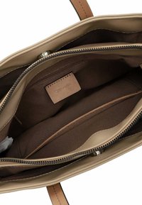 Intérieur d'un sac à main beige avec une doublure marron clair, comprenant un compartiment zippé, un emplacement pour cartes et un patch logo. Matériau lisse et durable.
