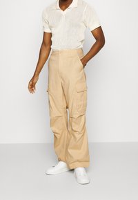 Beige cargobyxor gjorda av lättviktstyg har sidofickor, en avslappnad passform och ett något avsmalnat ben. Kombinerat med vita sneakers.