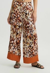 Losse, gestreepte broek van een zachte stof met bruine en beige luipaardvlekken; heeft een effen oranje zoom en zijzakken.