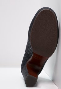 Zapato negro con patrón, con una parte superior texturizada, suela marrón y un ligero tacón. Presenta un diseño limpio y un acabado suave.