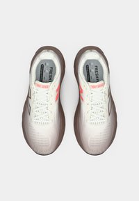 Une paire de chaussures de course blanches et brunes avec un logo et des lacets corail, vue de dessus sur un fond blanc uni.