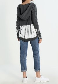 Szara bluza z kapturem w stylu tie-dye z białą dolną częścią, luźny krój. Połączona z podwiniętymi niebieskimi dżinsami i białymi butami.
