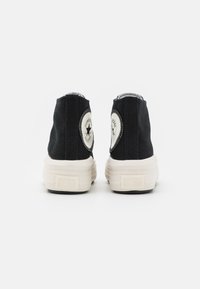 Czarne lniane sneakersy za kostkę z białą gumową podeszwą, z okrągłymi łatkami z logo na piętach i kontrastowym szwem na górze.