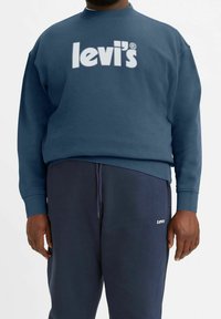 Felpa girocollo blu navy realizzata in tessuto morbido con logo bianco "Levi's". Abbinata a pantaloni della tuta blu scuro con un piccolo logo.