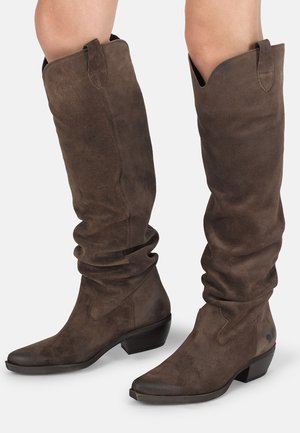 Brune ruskind knæhøje støvler med et slouchy design, spids tå og lav stablet hæl. Har diskrete stikninger som accent.
