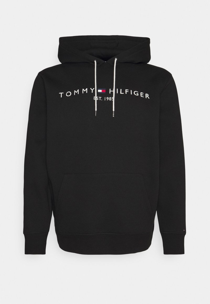 Sweat à capuche noir avec cordons blancs, poche avant, et texte "Tommy Hilfiger Est. 1985" avec un petit logo drapeau rouge, blanc et bleu sur la poitrine.