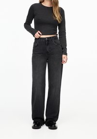 Black long-sleeve crop top and high-waisted black wide-leg jeans, featuring a smooth texture and subtle stitching details. Black shoes complete the outfit.