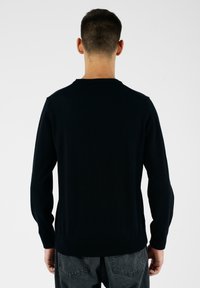 Maglione nero a maglia con scollatura rotonda, maniche lunghe e orlo aderente. Il tessuto appare liscio e leggero.
