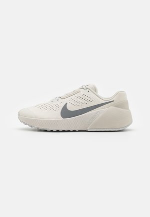 Zapatillas Nike de color beige claro con parte superior perforada, acentos grises, punta redondeada y suela gruesa y acolchada. Presenta el logo en el lateral.