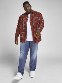 Crvena i crna košulja od flanela s bijelim naglascima preko bijele majice, uparena s plavim trapericama i bijelim tenisicama.