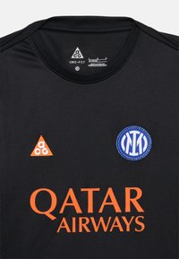 Μαύρη αθλητική φανέλα με πορτοκαλί λογότυπο "Qatar Airways", πορτοκαλί τρίγωνο λογότυπο ACG και μπλε κυκλικό έμβλημα στο στήθος.