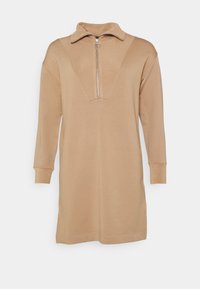 Beige Pullover-Kleid mit einem Viertelreißverschluss-Kragen, langen Ärmeln und einer lockeren Passform. Besitzt ein gesticktes V-Muster auf der Vorderseite. Weiche Stofftextur.
