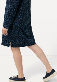 Navyblaues Kleid mit Leopardenmuster, langen Ärmeln und seitlichem Schlitz, kombiniert mit navyblauen Sneakers mit weißen Akzenten.