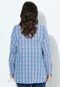 Blusa a quadri blu chiaro e grigia con maniche lunghe, tessuto testurizzato e polsini annodati. La parte posteriore presenta una vestibilità morbida.