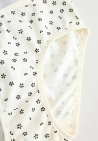 Tessuto crema chiaro con piccoli motivi floreali neri, texture morbida, scollatura rotonda e bordi cuciti. Progettato come un indumento aderente.