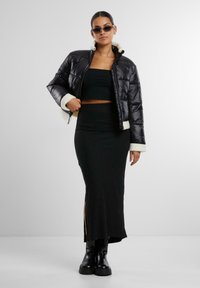Doudoune noire avec bordure en fourrure blanche, design court, associée à un ensemble noir fitted en deux pièces et des bottes noires à hauteur de genoux.