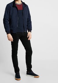 Laivastonsininen bomber-takki mustalla vetoketjulla, yhdistettynä viininpunaiseen ja laivastonsiniseen raidalliseen t-paitaan, mustiin pillifarkkuihin ja laivastonsinisiin lenkkareihin, joissa on vaaleanruskeat pohjat.