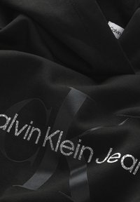 Hoodie nera con logo lucido Calvin Klein Jeans in texture contrastanti di argento e nero, con una vestibilità moderna e un tessuto morbido.