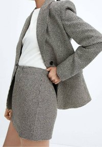 Ensemble blazer et jupe en houndstooth noir et blanc, design structuré, tissu texturé, avec épaulettes et une poche dans la jupe.