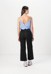 Top sans manches à motifs bleus avec un dos en V, associé à un jean large taille haute noir, terminé par un ourlet effiloché. Baskets légères aux pieds.