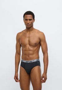 Černé sportovní slipy se šedým vzorovaným pasem, na kterém je logo Nike. Tkanina působí hladce a elasticky, navržená pro pohodlí a oporu.