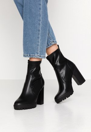 Sorte ankelstøvler i glat læder, med afsmalnet silhuet, robust blokhæl og tekstureret, mønstret sål. Båret med korte blå denim.
