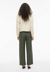 Beige kabelgebreide trui met een cropped ontwerp, gedragen met groene wijde broek. Zachte textuur en ontspannen silhouet.