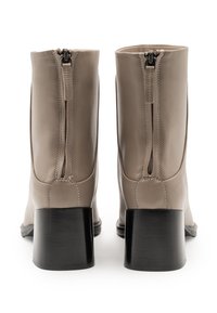 Stivali alla caviglia in pelle beige con tacco quadrato nero, dotati di una cerniera posteriore e di una texture liscia. Design semplice senza decorazioni.