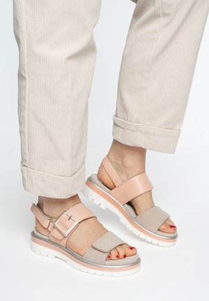 Füße in beigen und rosa offenen Sandalen mit weißen Sohlen, kombiniert mit hochgekrempelten, hellen Cordhosen.
