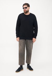 Granatowy sweter dzianinowy z teksturowanym wzorem, szare dżinsy o szerokich nogawkach i czarne tenisówki. Okulary przeciwsłoneczne dopełniają strój.