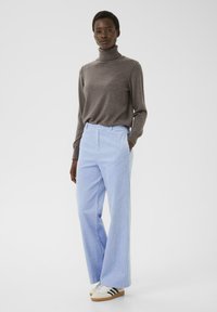 Grijze coltrui, lichtblauwe gestreepte wijde broek en witte sneakers met zwarte accenten, weergegeven tegen een eenvoudige achtergrond.