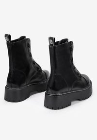 Botas de tobillo de cuero negro con suela gruesa, diseño de cordones y costuras detalladas. Presentan una tira en la parte trasera y un acabado suave y brillante.