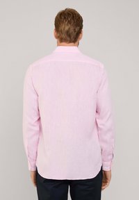 Camisa de manga larga en tejido de un suave color rosa claro, con un sutil texturizado, que presenta un cuello estándar y puños con botones, combinada con pantalones oscuros.