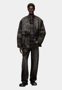 Completo in denim nero con giacca loose e pantaloni dritti caratterizzati da una finitura tessurizzata sottile. La persona indossa scarpe massicce nere.