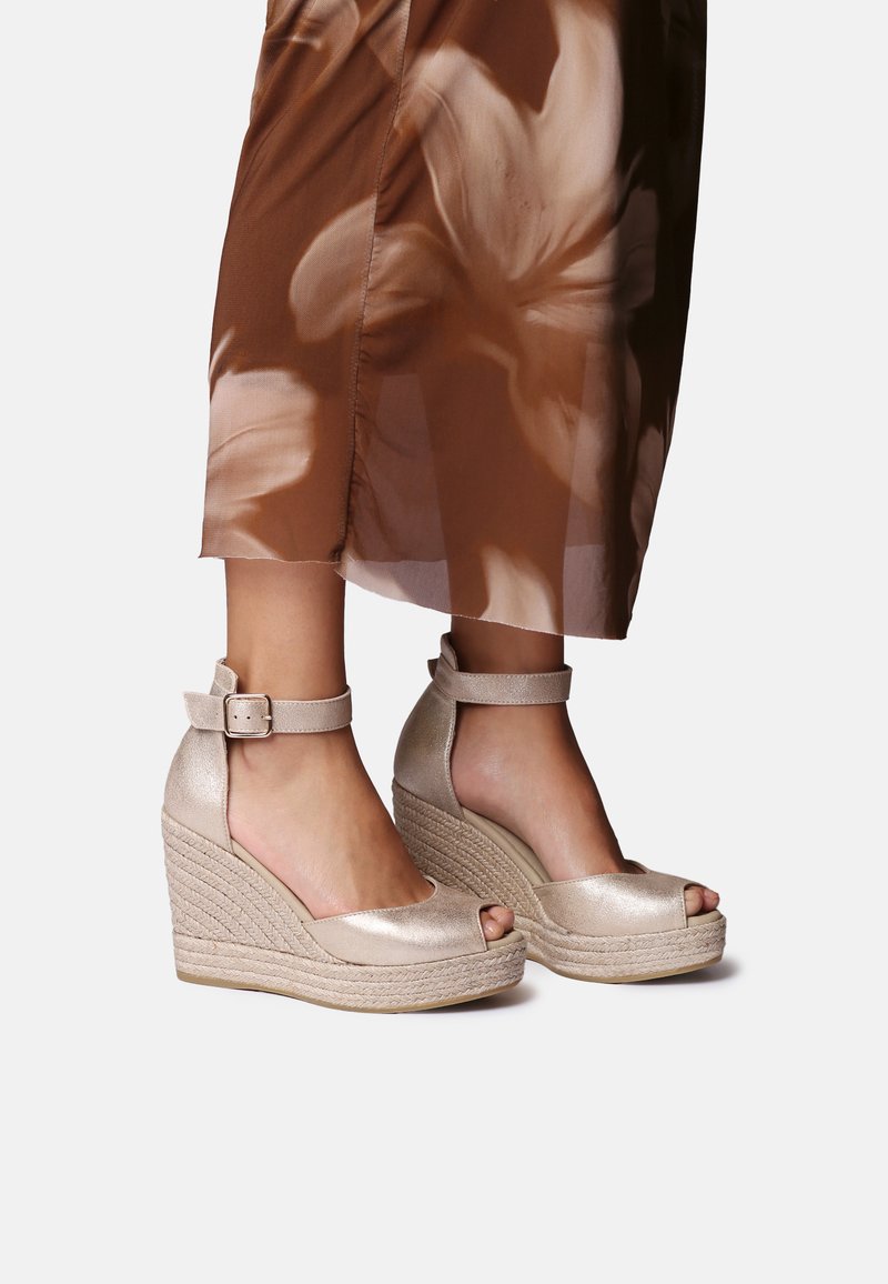 Wedge sandals with a metallic gold finish, open toe design, and ankle strap. Jute midsole adds texture; smooth, sleek surface.