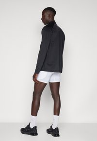 Camiseta deportiva negra de manga larga, pantalones cortos blancos y zapatillas negras. Tela suave, ajuste relajado, diseño minimalista sin logotipos ni patrones visibles.