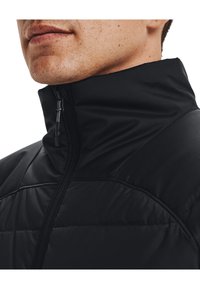 Czarna pikowana kurtka z wysokim kołnierzem, wyposażona w przedni zamek błyskawiczny i gładką, lekką teksturę. Design jest minimalistyczny i dopasowany.