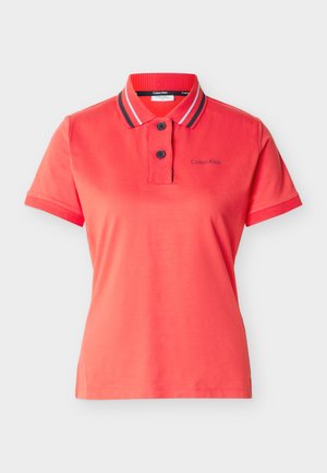 Polo rouge à manches courtes avec deux boutons noirs et col rayé, arborant un petit logo "Calvin Klein" sur la poitrine gauche.