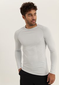 Langärmeliges, hellgraues Sportshirt aus elastischem Material, mit strukturierten Seitenpaneelen und kleinen Perforationen für Atmungsaktivität.