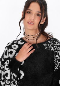 Maglione fuzzy in bianco e nero con un design a stampa leopardata, maniche larghe e vestibilità oversize. Collane choker di perline multiple attorno al collo.