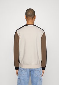 Sudadera de cuello redondo con un cuerpo beige y acentos marrones, negros y marinos en las mangas, fabricada en suave tela de algodón.