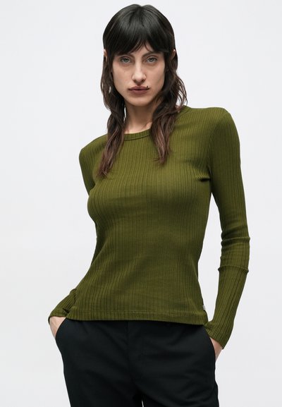 Ριμπ μακρυμάνικη μπλούζα σε ελιά πράσινο, φτιαγμένη από απαλό ύφασμα. Διαθέτει στρογγυλή λαιμόκοψη και εφαρμοστή σιλουέτα, με διακριτική υφή.